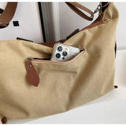 Borsa a tracolla in tela beige con tasca esterna, cerniera in pelle marrone e smartphone visibile. Accessorio moda casual e pratico.
