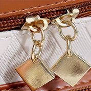 Cerniera in metallo dorato con pendenti quadrati su borsa in pelle marrone. Accessori moda eleganti, dettagli di lusso, chiusura resistente.