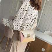 Donna con camicia a pois indossa borsa a tracolla multicolore geometrica, manico dorato, catena elegante. Accessorio moda femminile trendy.