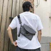 Uomo con borsa a tracolla grigia, indossa t-shirt bianca e cappellino nero. Moda casual urbana, accessorio pratico e moderno.