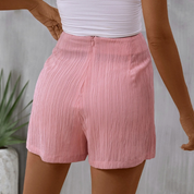 Shorts rosa a vita alta in tessuto plissettato, indossati da una donna. Moda estiva, abbigliamento casual femminile, stile elegante e confortevole.