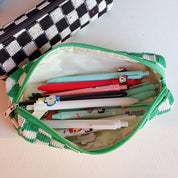Astuccio verde a quadretti aperto con penne colorate su tavolo bianco. Accessori scolastici, cancelleria per studenti, organizzazione ufficio.