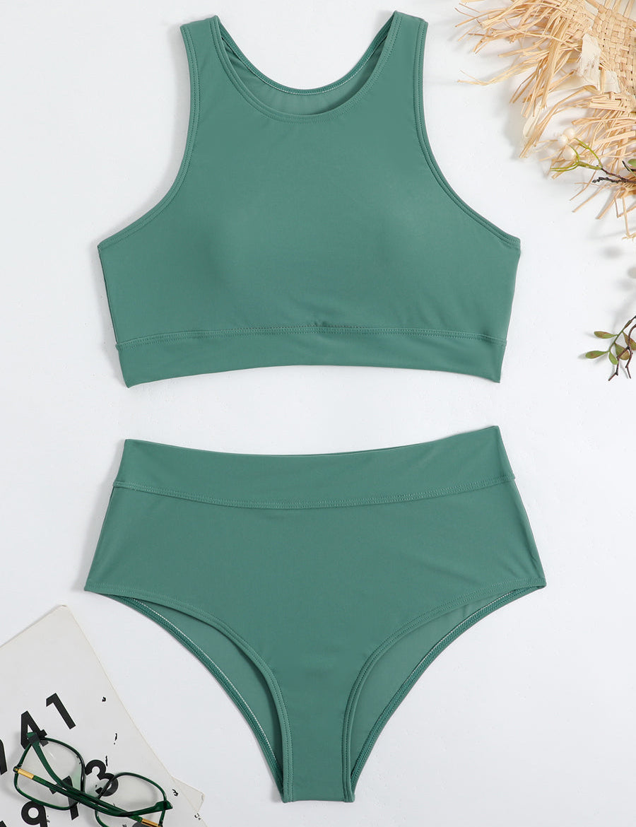 Costume da bagno verde a due pezzi, top sportivo e slip a vita alta, su sfondo bianco con occhiali e accessori estivi.