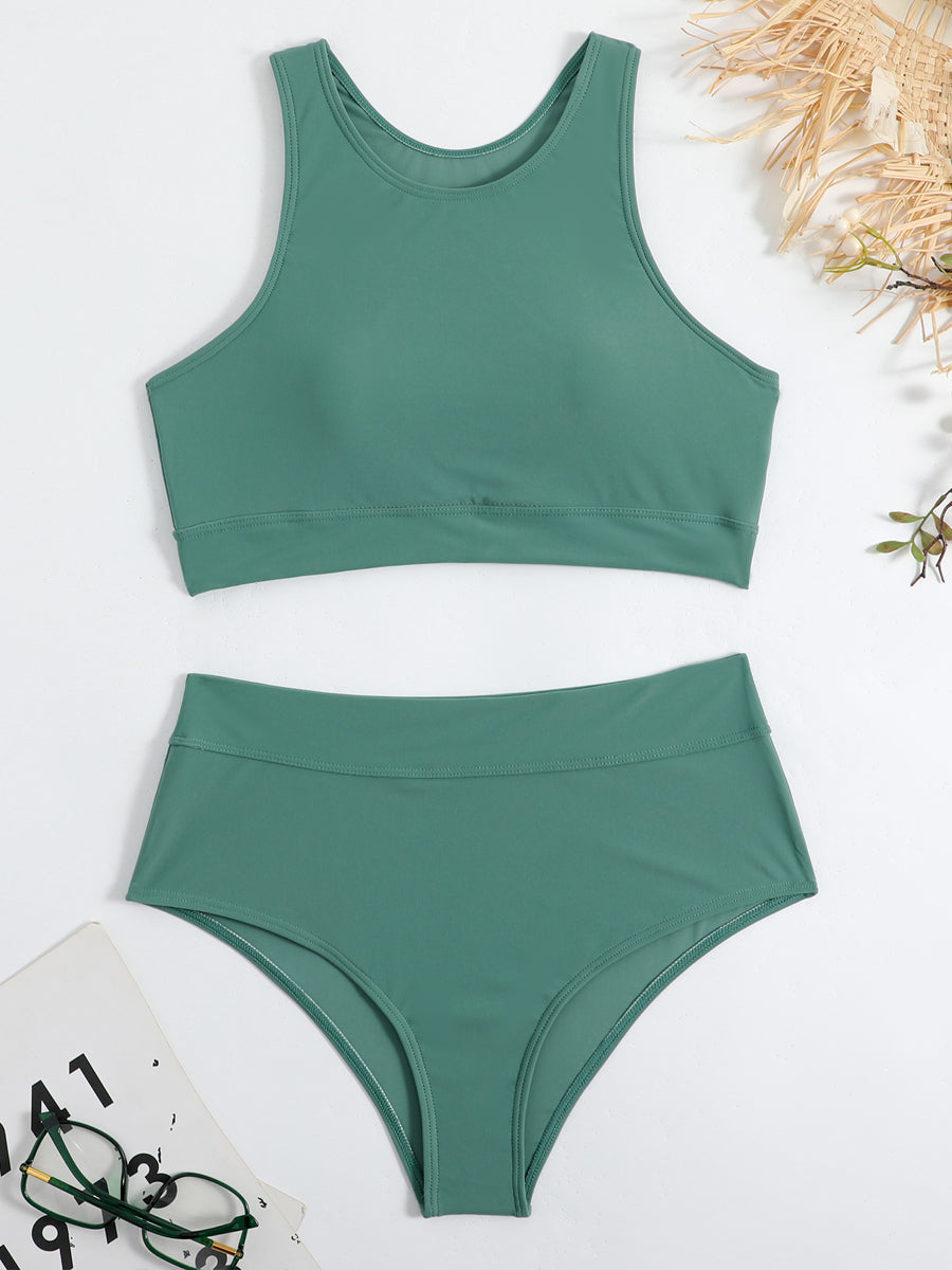 Costume da bagno verde a due pezzi, top sportivo e slip a vita alta, su sfondo bianco con occhiali e accessori estivi.