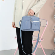Borsa a tracolla unisex blu, design moderno con doppie tasche frontali, indossata da una persona in giacca beige. Accessorio moda versatile.