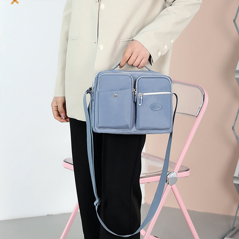 Borsa a tracolla unisex blu, design moderno con doppie tasche frontali, indossata da una persona in giacca beige. Accessorio moda versatile.