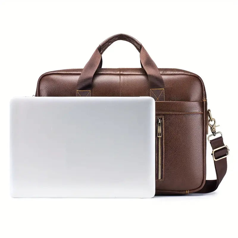 Borsa da lavoro in pelle marrone con tracolla regolabile, tasca frontale con zip, accanto a un laptop argento. Elegante e funzionale per ufficio.