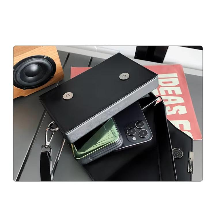 Borsa a tracolla nera in pelle con chiusura magnetica, smartphone e libro su tavolo moderno. Accessorio moda elegante e funzionale.