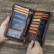 Portafoglio da viaggio in pelle marrone con passaporto USA, penna e scomparti per carte su tavolo in legno. Accessorio elegante e funzionale.