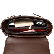 Interno di una borsa a tracolla in pelle marrone con scomparti, contenente un portafoglio, un libro e un rossetto. Accessori moda donna eleganti.