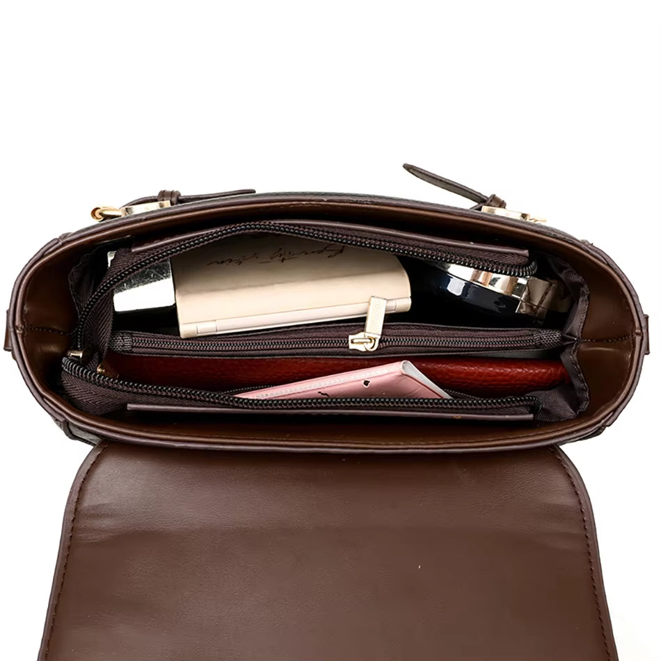 Interno di una borsa a tracolla in pelle marrone con scomparti, contenente un portafoglio, un libro e un rossetto. Accessori moda donna eleganti.