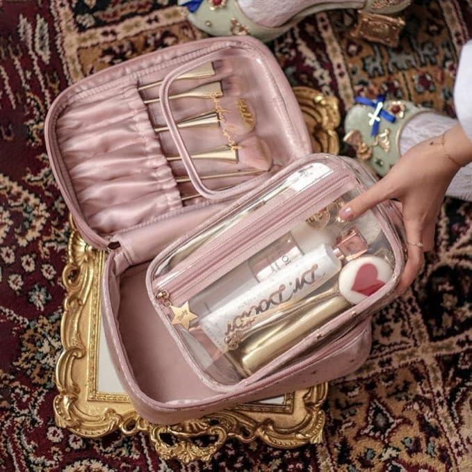 Set di trucchi rosa su tappeto decorativo, include pennelli e custodia trasparente con cosmetici. Elegante e pratico per viaggi e organizzazione.
