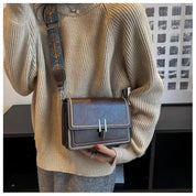 Donna con maglione beige indossa borsa a tracolla marrone in pelle con chiusura metallica, tracolla decorata. Elegante accessorio moda autunno.