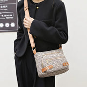 Borsa a tracolla beige con motivo geometrico, dettagli in pelle marrone e cerniere dorate, indossata da una persona in cappotto nero.