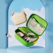 Astuccio da viaggio verde aperto con accessori per trucco, specchio e tasca a rete, accanto a borsa beige con manico, sfondo cielo blu.