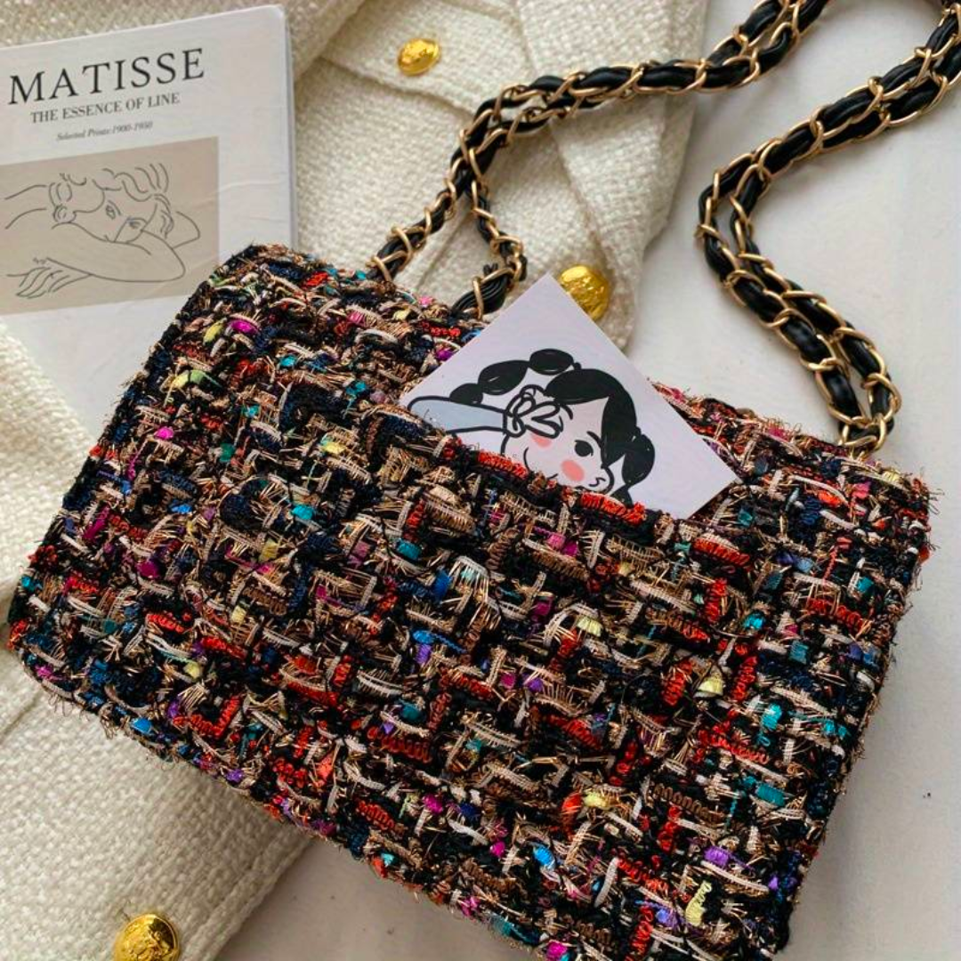Borsa a tracolla in tessuto tweed multicolore su cappotto bianco con bottoni dorati, catena dorata intrecciata, libro di Matisse sullo sfondo.