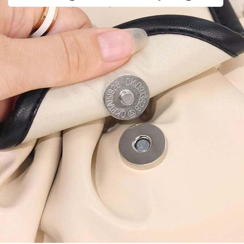Mano che apre una borsa in pelle beige con chiusura magnetica in metallo. Design elegante, accessorio moda donna, dettagli di alta qualità.