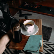 Tazza di caffè su vassoio di legno con passaporto verde e thermos nero, tastiera retroilluminata sullo sfondo. Viaggio, caffè, lavoro da remoto.