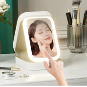 Specchio cosmetico LED con touch screen, illuminazione regolabile, design portatile, ideale per trucco e skincare, posizionato su tavolo da trucco.