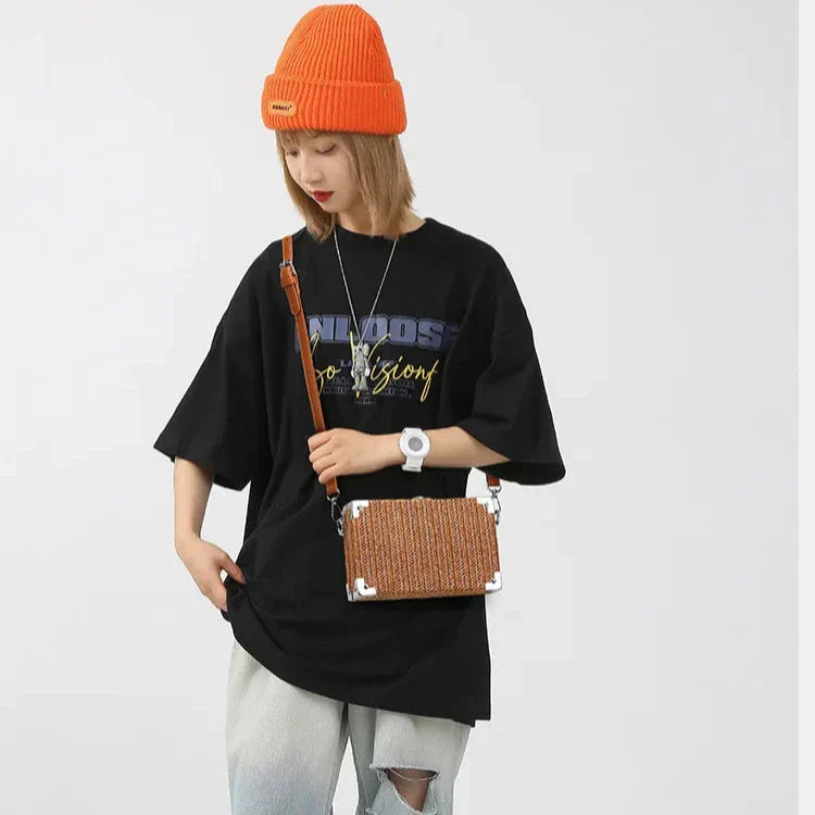 Giovane donna con maglietta nera oversize, jeans chiari, berretto arancione e borsa a tracolla marrone. Stile casual, moda urbana.