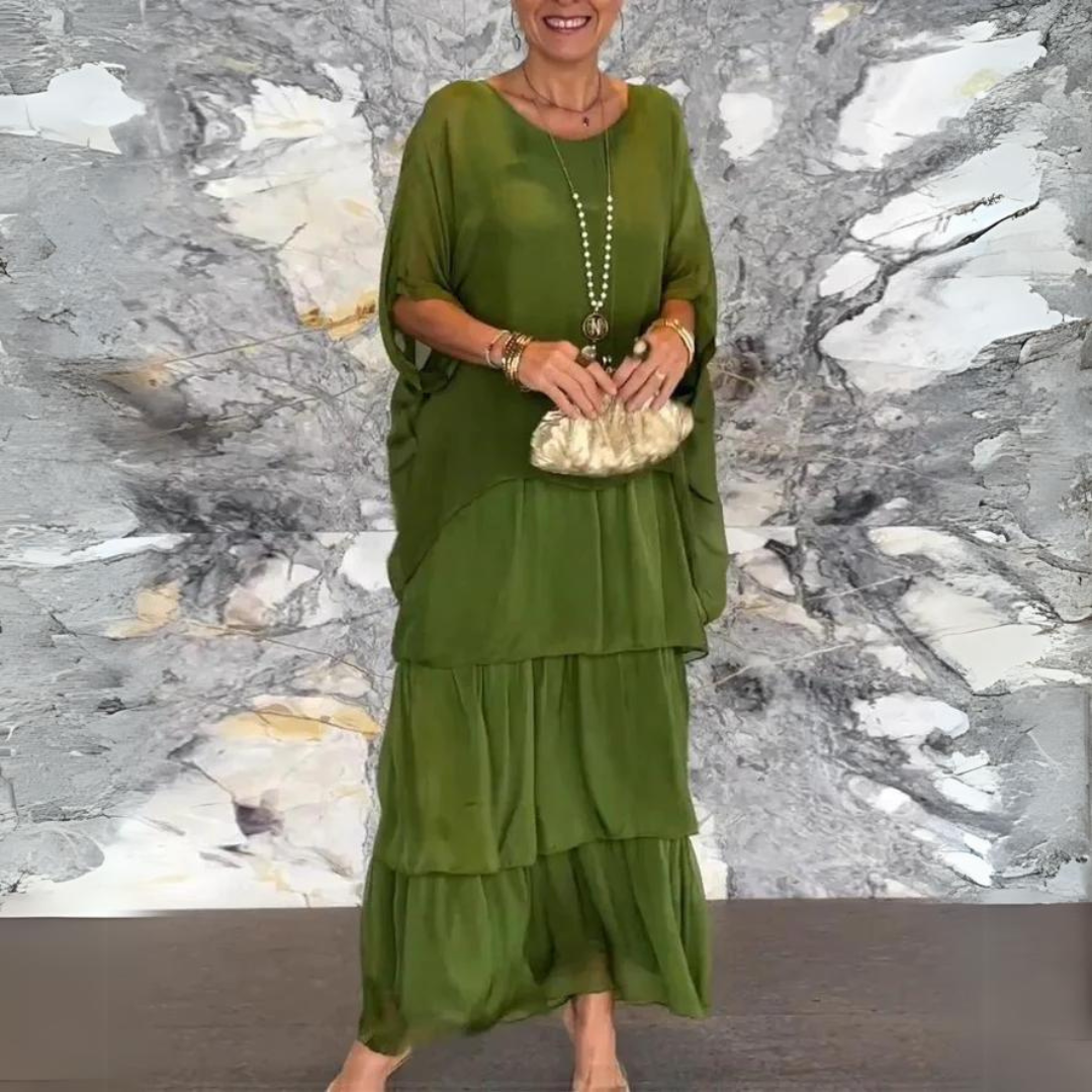 Abito lungo verde elegante, donna sorridente, sfondo marmo grigio, accessori oro, clutch dorata. Moda femminile, abbigliamento chic, stile sofisticato.
