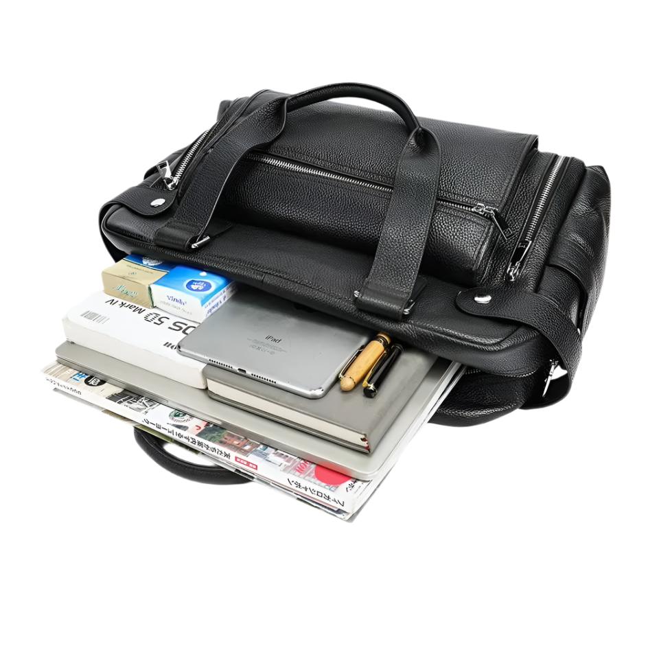 Borsa ventiquattrore in pelle nera con scomparti aperti, contenente laptop, tablet, penne, giornali e documenti. Elegante e funzionale per lavoro.