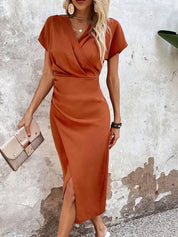 Donna con abito midi arancione elegante, clutch beige, orecchini pendenti, sfondo muro grigio. Moda femminile, abbigliamento estivo chic.