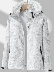 Giacca impermeabile donna bianca con cappuccio, motivo foglie tropicali, chiusura zip, tasche laterali, ideale per outdoor e sport.