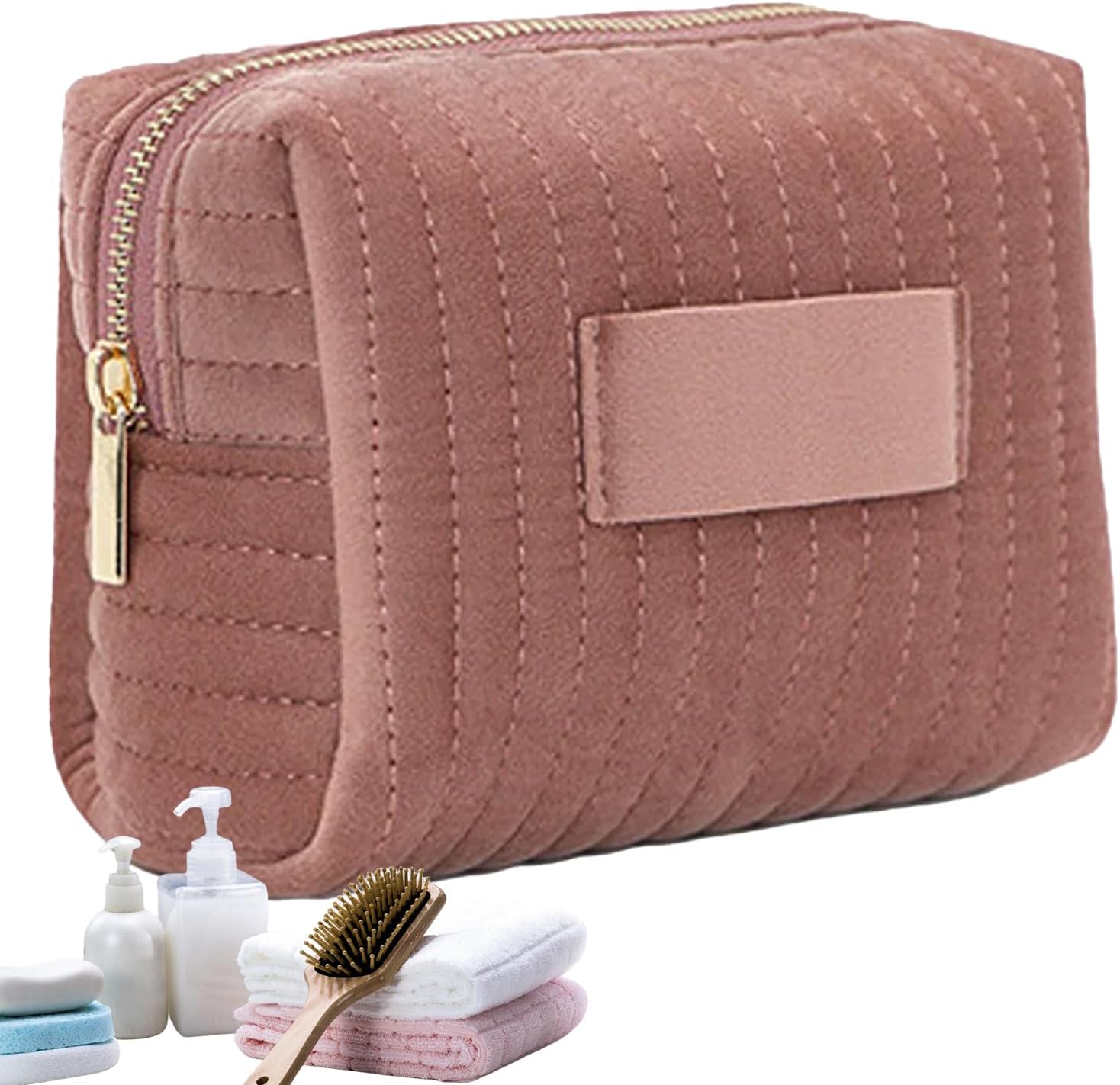 Astuccio cosmetico rosa trapuntato con cerniera dorata, accompagnato da asciugamani, spazzola e flaconi. Accessorio da viaggio elegante e pratico.
