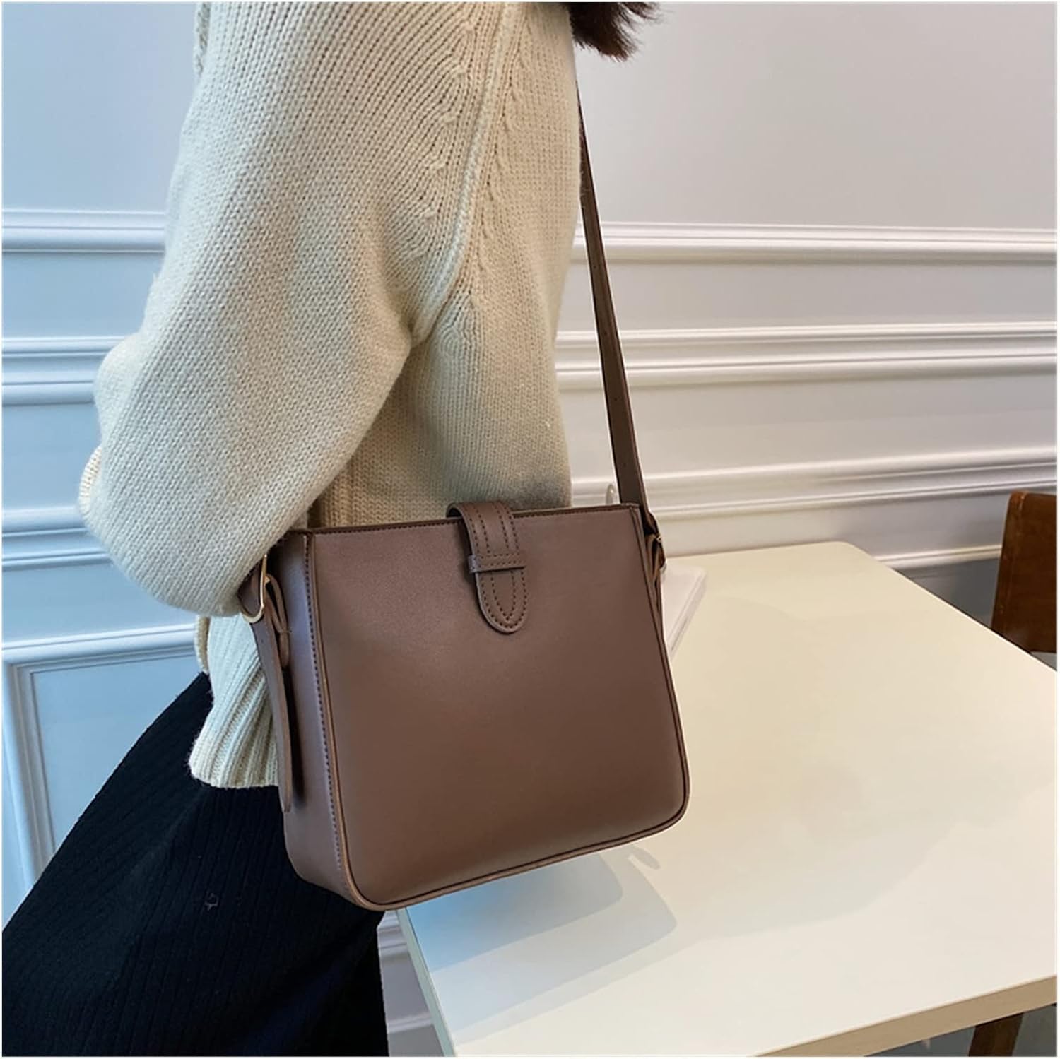 Borsa a tracolla marrone in pelle, design minimalista, indossata da una persona con maglione beige. Accessorio moda elegante per donna.