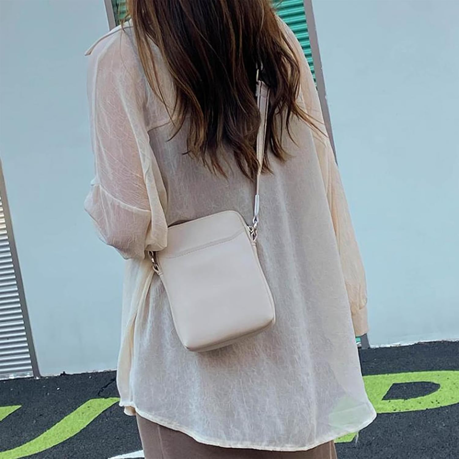 Donna con camicia trasparente beige e borsa a tracolla bianca. Moda femminile, accessori eleganti, stile casual.