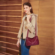 Donna con giacca beige e borsa a tracolla in pelle bordeaux, sfondo in legno. Accessorio moda elegante, stile casual chic.