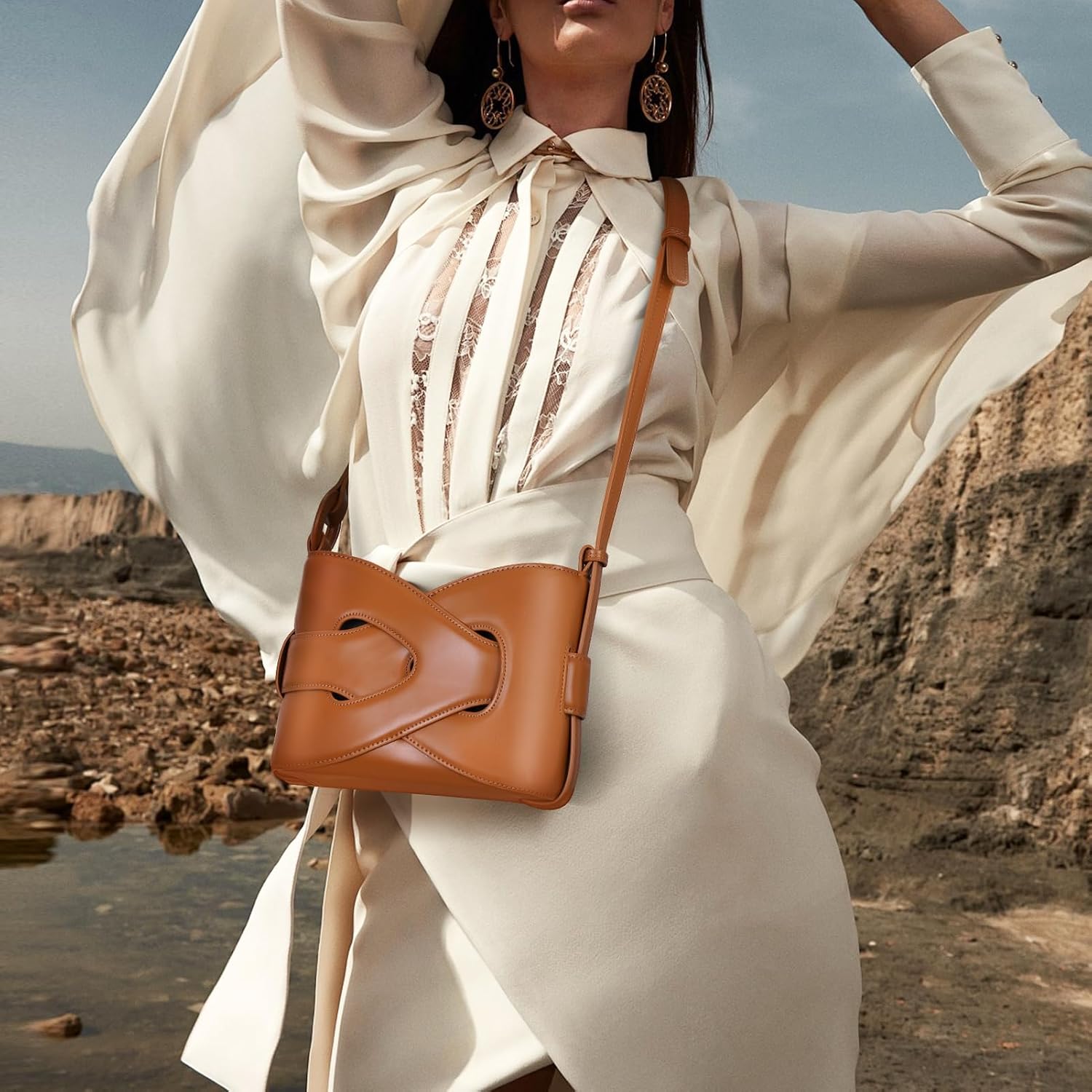 Borsa a tracolla in pelle marrone su sfondo naturale, indossata da modella in abito bianco elegante. Accessorio moda donna, stile chic e sofisticato.