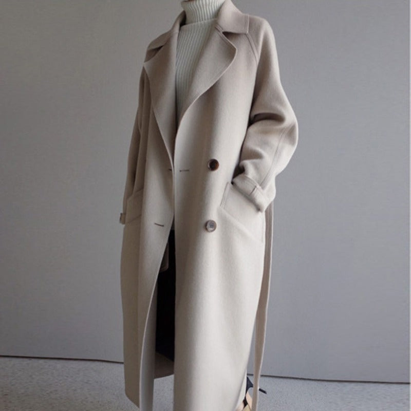 Cappotto lungo beige da donna, elegante e invernale, con cintura e bottoni, perfetto per look casual e formali. Tessuto caldo e morbido.