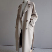 Cappotto lungo beige da donna, elegante e invernale, con cintura e bottoni, perfetto per look casual e formali. Tessuto caldo e morbido.