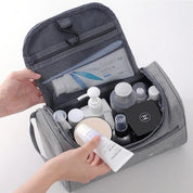 Borsa da toilette grigia aperta con vari prodotti cosmetici e per la cura della pelle, tra cui flaconi e creme. Organizzatore da viaggio pratico e capiente.