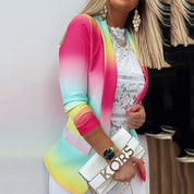 Giacca donna multicolore sfumata, indossata su top in pizzo bianco. Accessori: borsa bianca con logo dorato, orologio nero, orecchini pendenti.