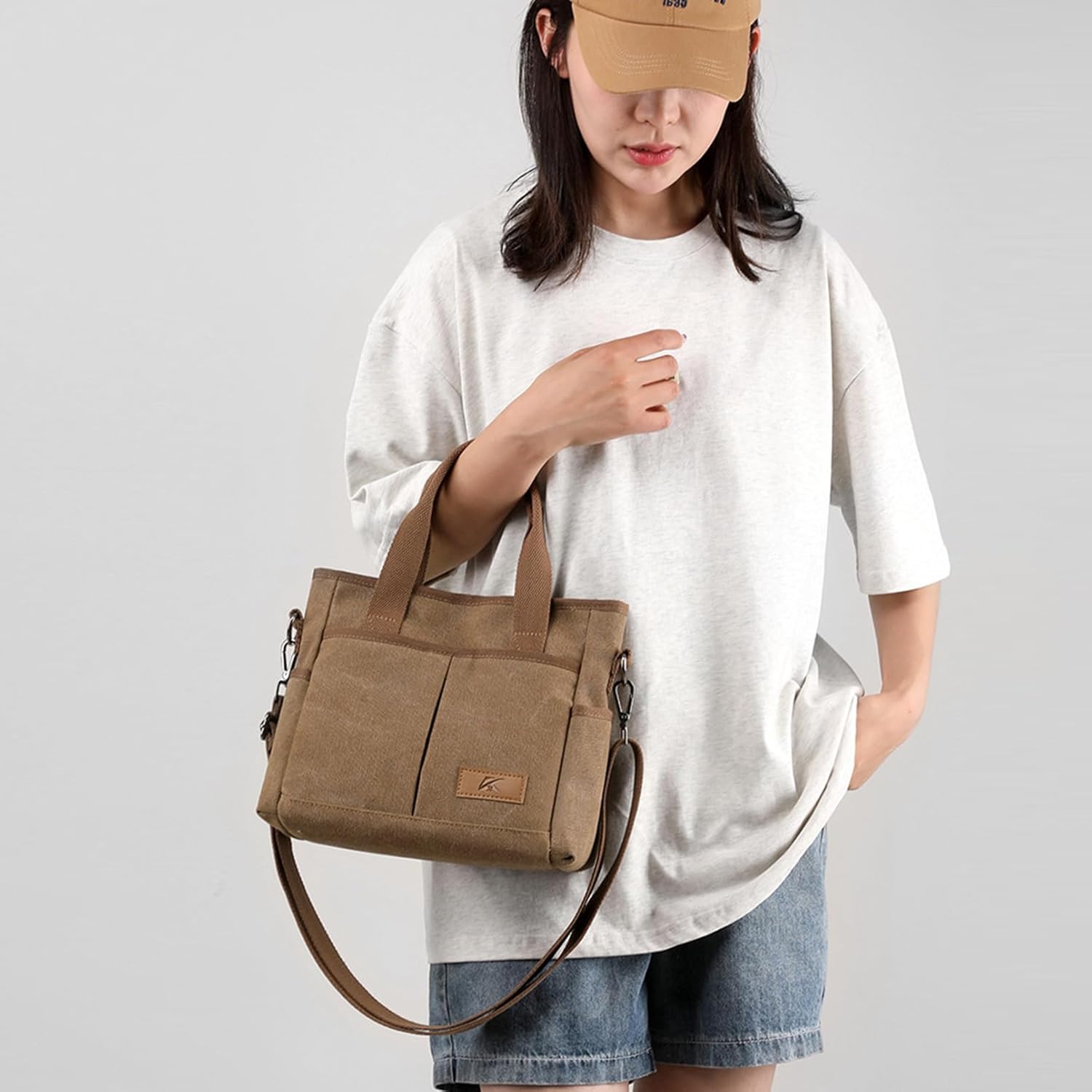 Donna con borsa a tracolla in tela beige, design casual, indossa maglietta bianca e cappellino. Moda donna, accessori pratici e versatili.