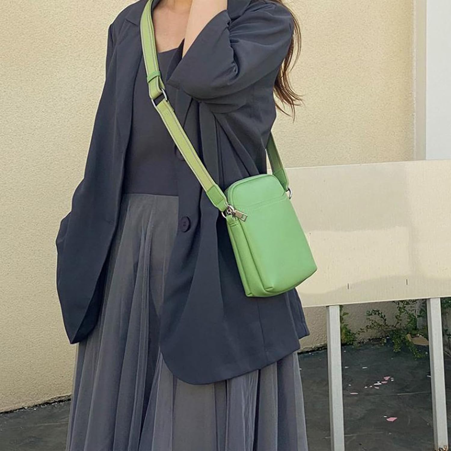 Donna con borsa a tracolla verde, indossa giacca e gonna grigia. Moda femminile elegante, accessori trendy, abbigliamento casual chic.