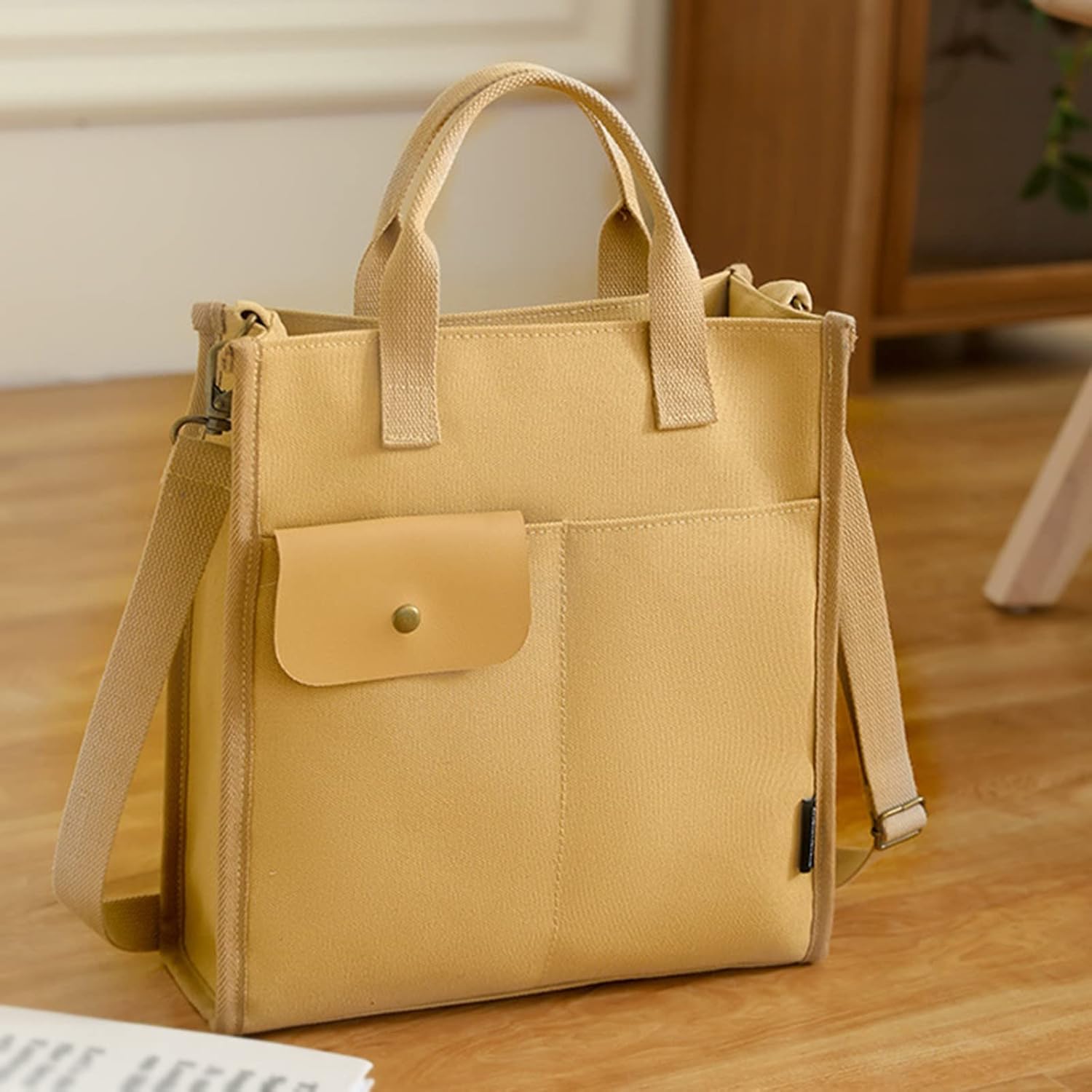 Borsa tote in tela beige con tasca frontale e tracolla regolabile, design minimalista, ideale per uso quotidiano e shopping.