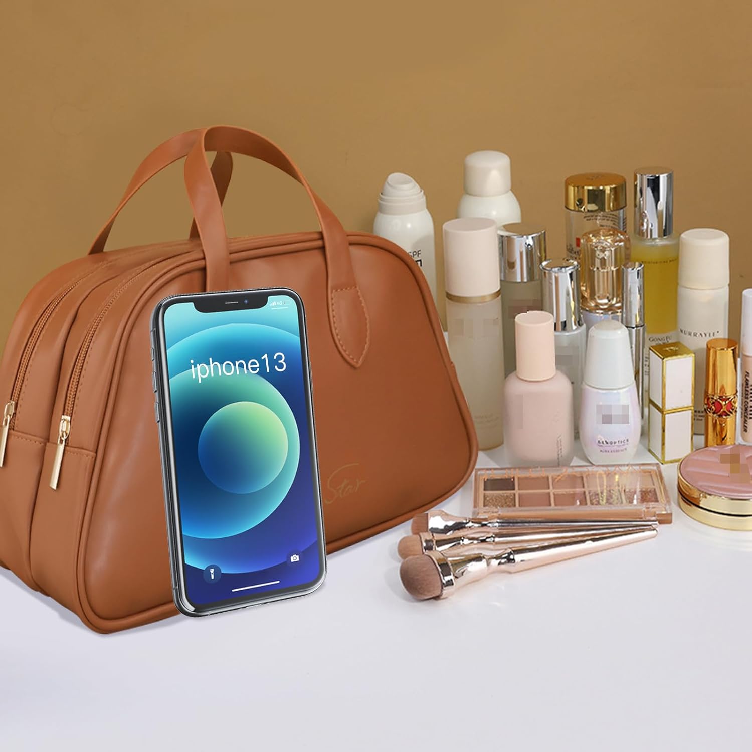 Borsa cosmetica marrone con iPhone 13, prodotti di bellezza e pennelli trucco su sfondo beige. Accessori moda e tecnologia.
