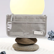 Pochette trasparente grigia su pietre, design minimalista, ideale per viaggi. Accessorio moda elegante, pratico e versatile.