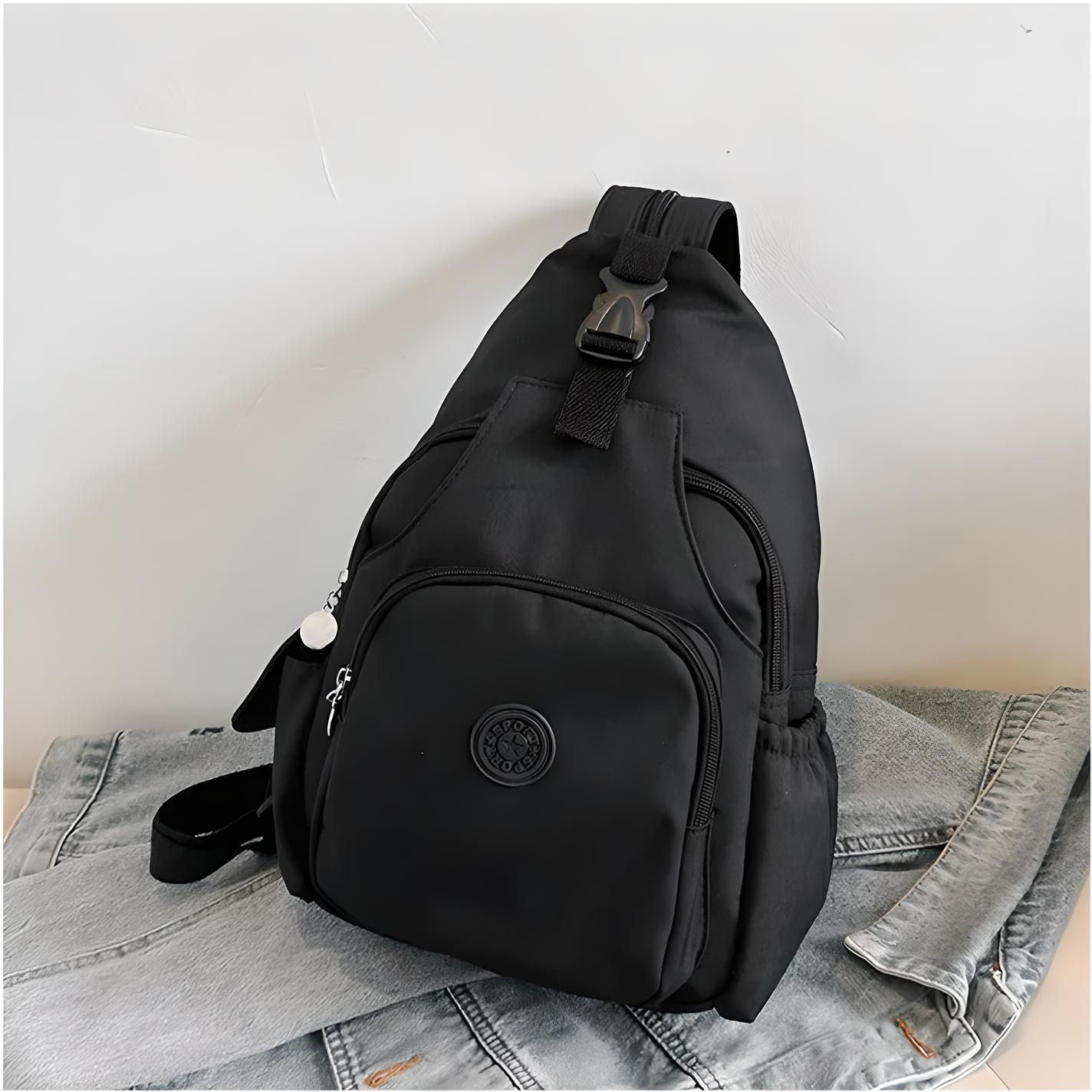 Zaino nero a tracolla su giacca di jeans, design moderno, tasche multiple, chiusura a zip, ideale per viaggi e uso quotidiano.