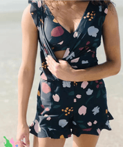 Utente in spiaggia indossa tuta corta floreale nera, senza maniche, con scollo a V. Abbigliamento estivo donna, moda mare, stile casual.