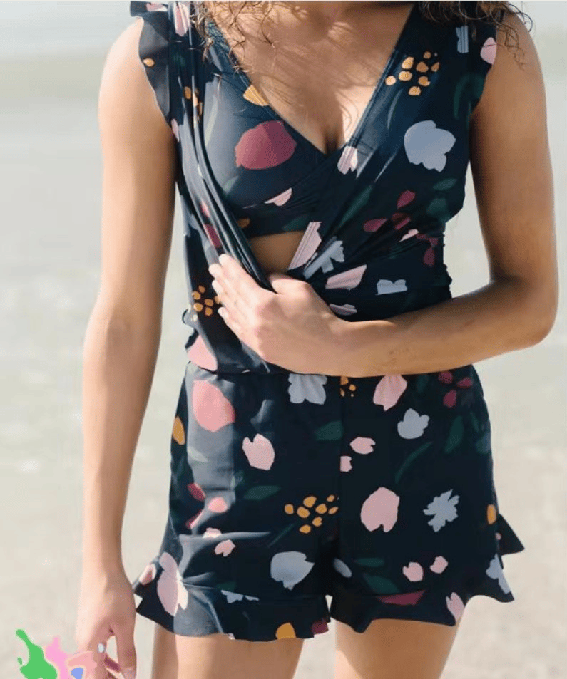 Utente in spiaggia indossa tuta corta floreale nera, senza maniche, con scollo a V. Abbigliamento estivo donna, moda mare, stile casual.