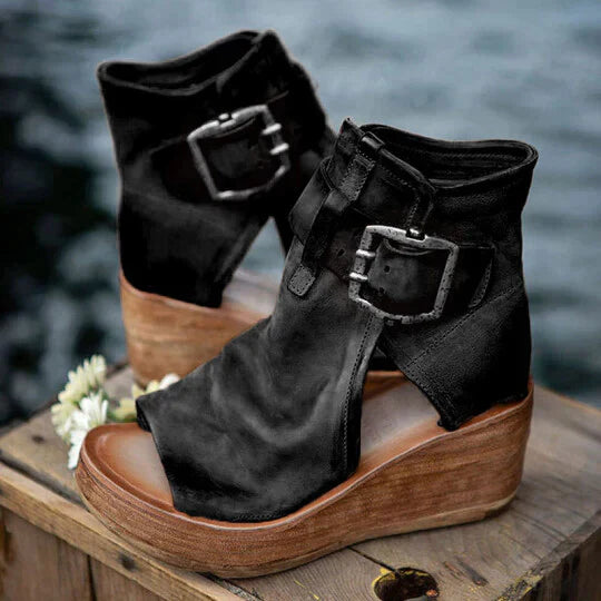 Sandali neri con zeppa in legno, fibbie decorative, design aperto, su tavolo di legno. Scarpe estive eleganti, moda donna.