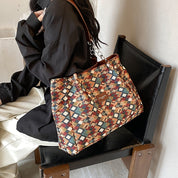 Borsa a tracolla multicolore con motivo geometrico, indossata da una persona seduta. Accessorio moda elegante, perfetto per ogni occasione.