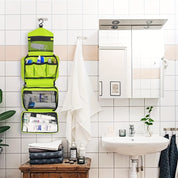 Organizer da bagno verde appeso, con scomparti per articoli da toeletta, su parete piastrellata bianca. Lavabo e specchio a destra.