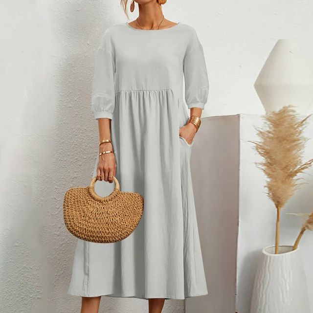 Abito lungo donna grigio chiaro, maniche a tre quarti, tasche laterali, stile casual. Accessori: borsa paglia, bracciali dorati. Moda estiva elegante.