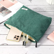 Astuccio verde in tessuto a coste con zip, contenente uno smartphone e un flacone di profumo. Accessorio moda pratico ed elegante per organizzare oggetti personali.